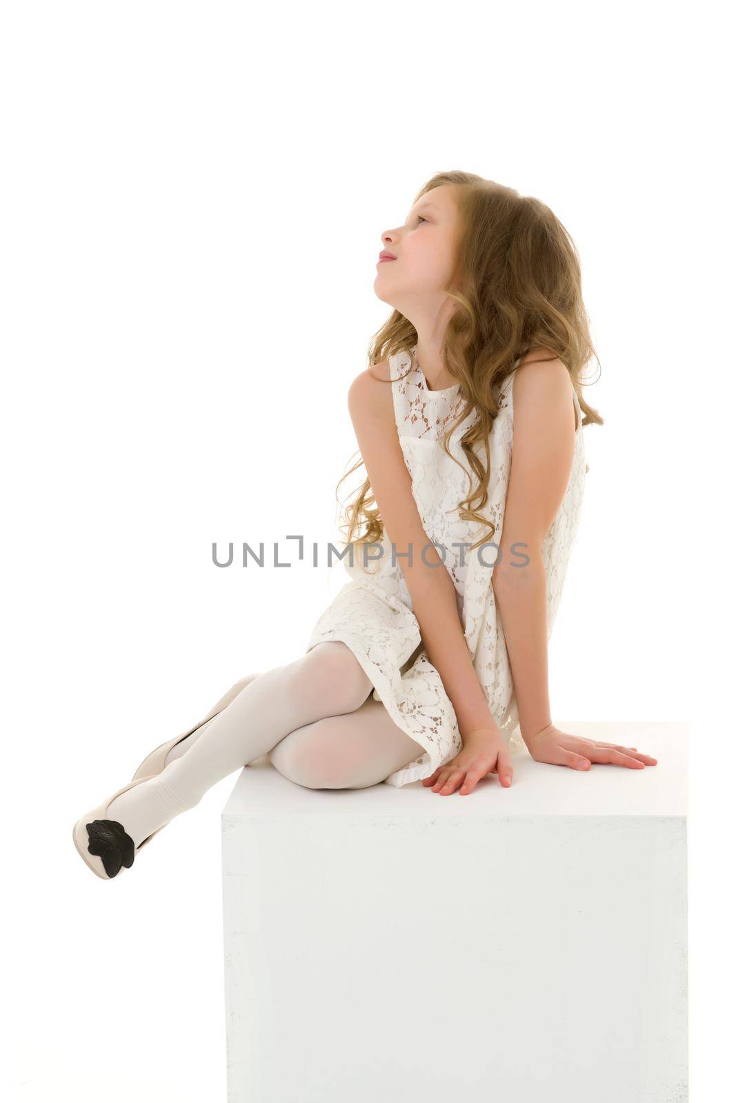 Beautiful Girl in White Lace Dress Sitting on Cube Looking to the Side, Portrait of Adorable Blonde Girl Wearing Trendy Stylish Clothes Posing in Studio Against White Background