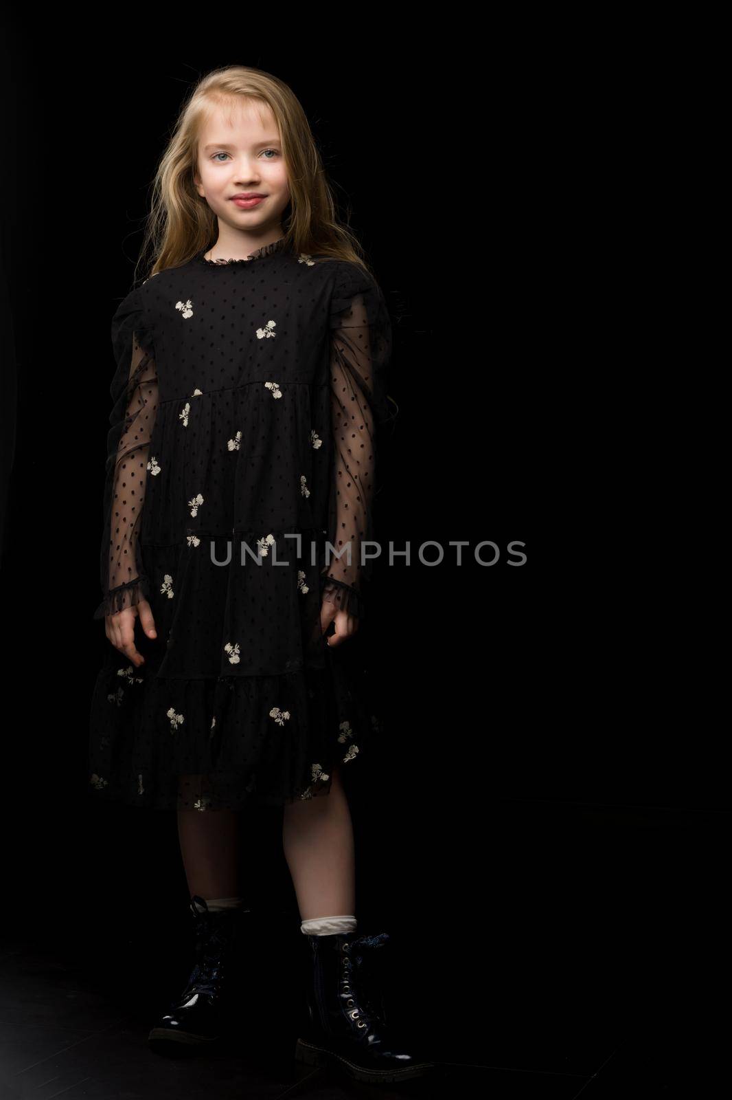 Cute little girl in a beautiful dress on a black background. Studio photo.