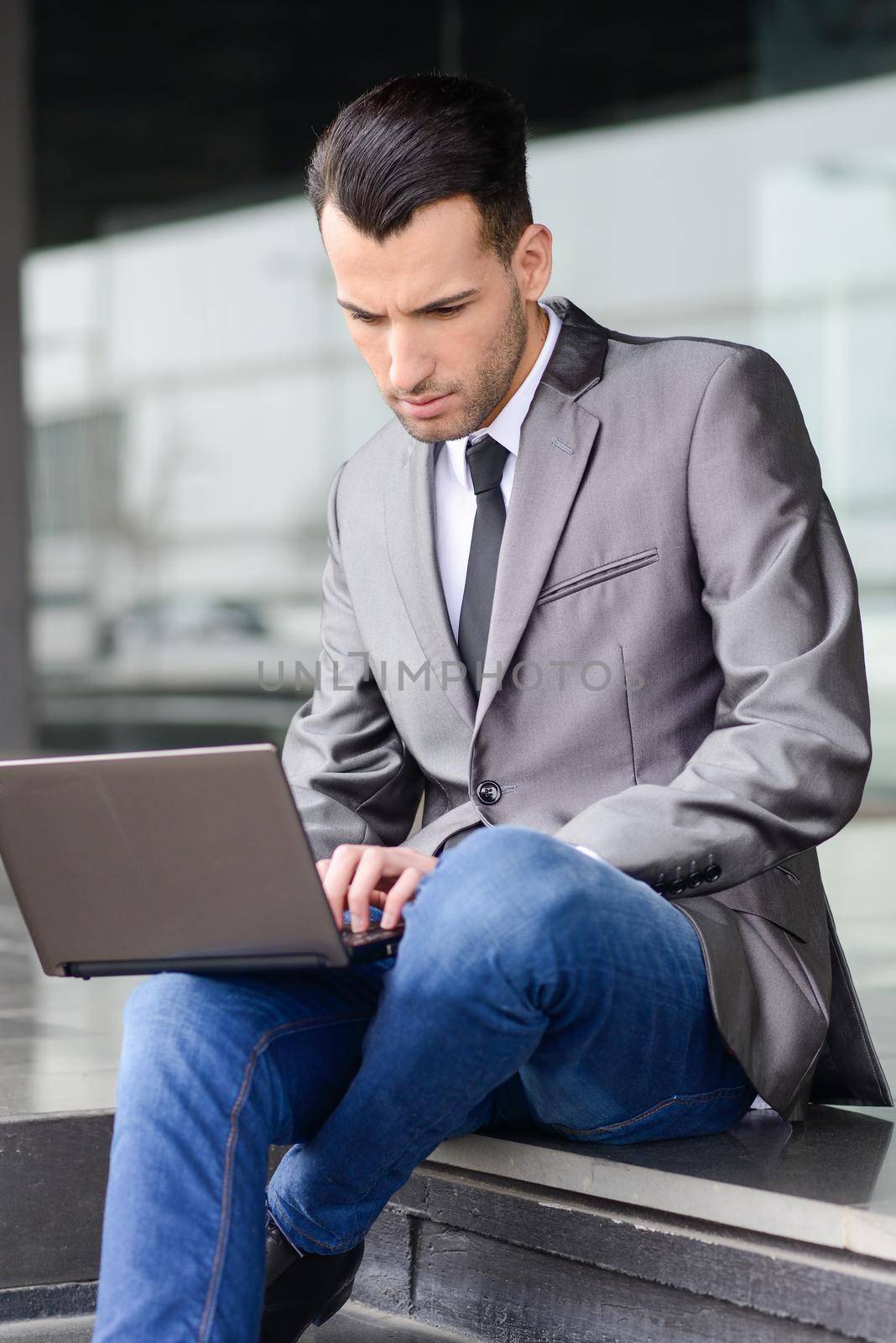 Young businessman typing in a laptop computer in urban background by javiindy