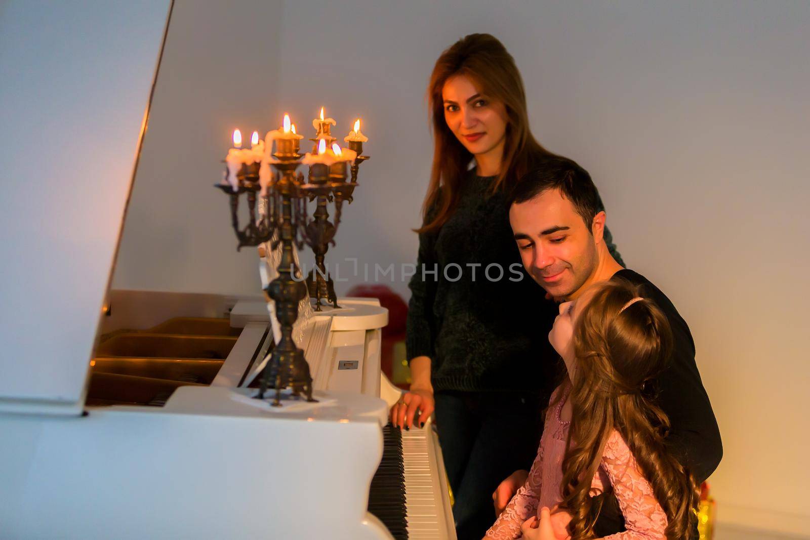 Happy Family Posing near Piano Decorated with Burining Candles by kolesnikov_studio