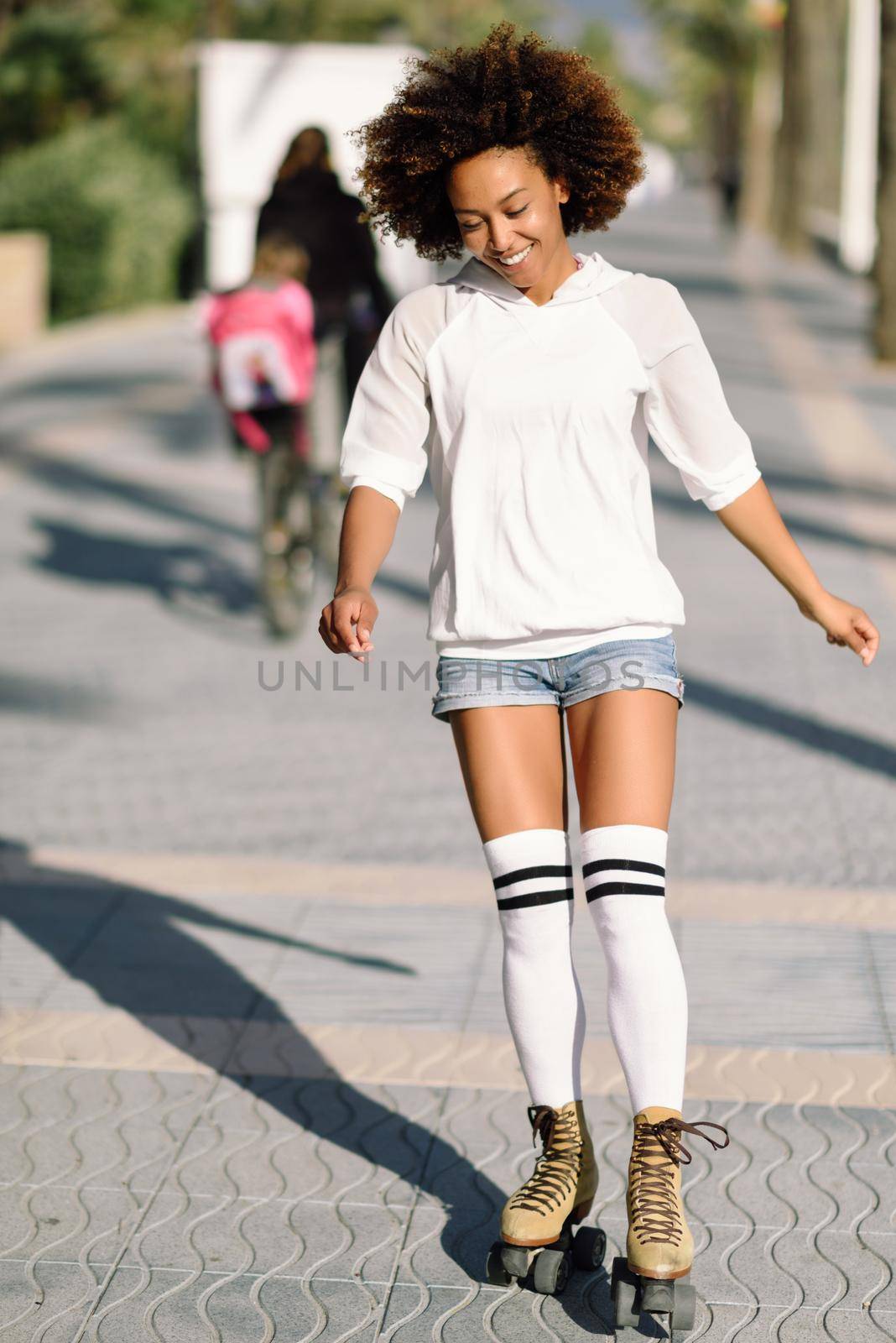 Smiling black woman on roller skates riding outdoors on beach promenade with palm trees. Smiling girl with afro hairstyle rollerblading on sunny day.