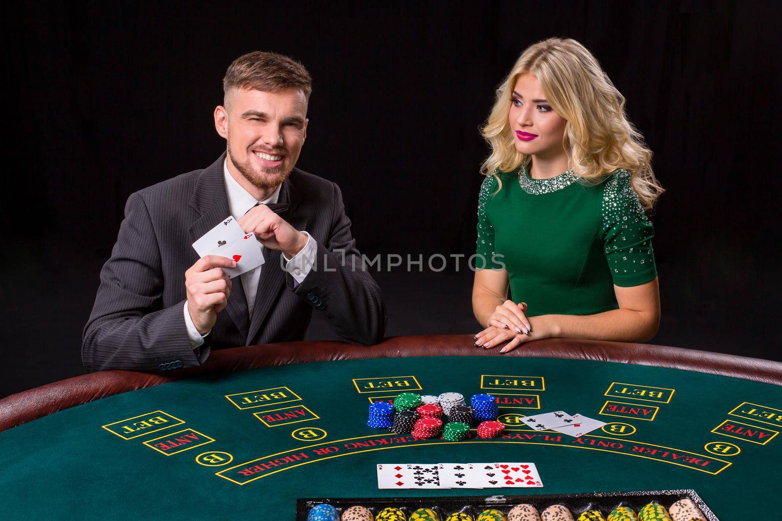 couple playing poker at the green table. The blonde girl and a guy in a suit. happy win, two aces