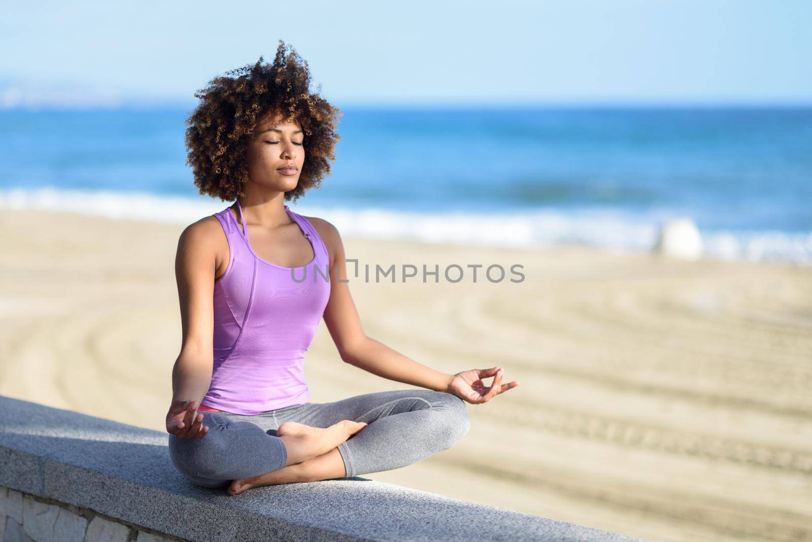 Black woman, afro hairstyle, in lotus pose with eyes closed in the beach by javiindy