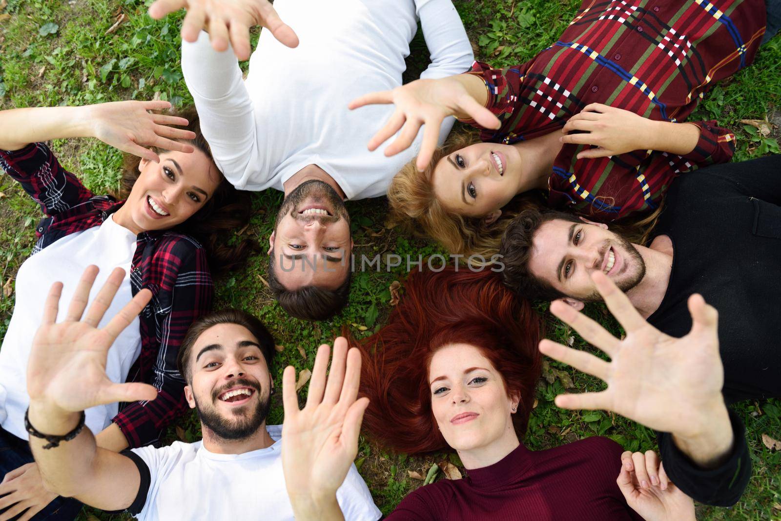 Women and men laying on grass wearing casual clothes. Group of young people together outdoors in urban park.