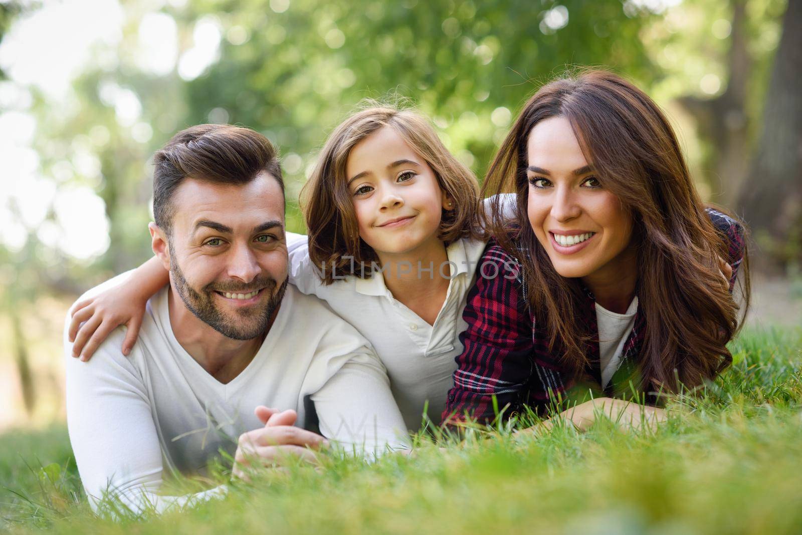 Happy young family in a urban park. Father, mother and little daughter laying on grass.