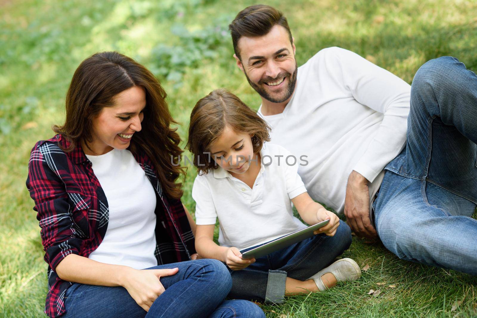 Happy family in a urban park playing with tablet computer by javiindy