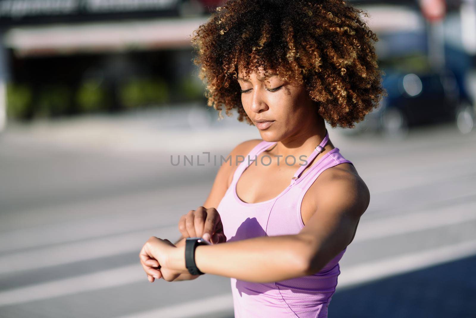 Young black woman using smartwatch touching touchscreen in active sports activity. Girl with afro hair looking at her smart watch screen.