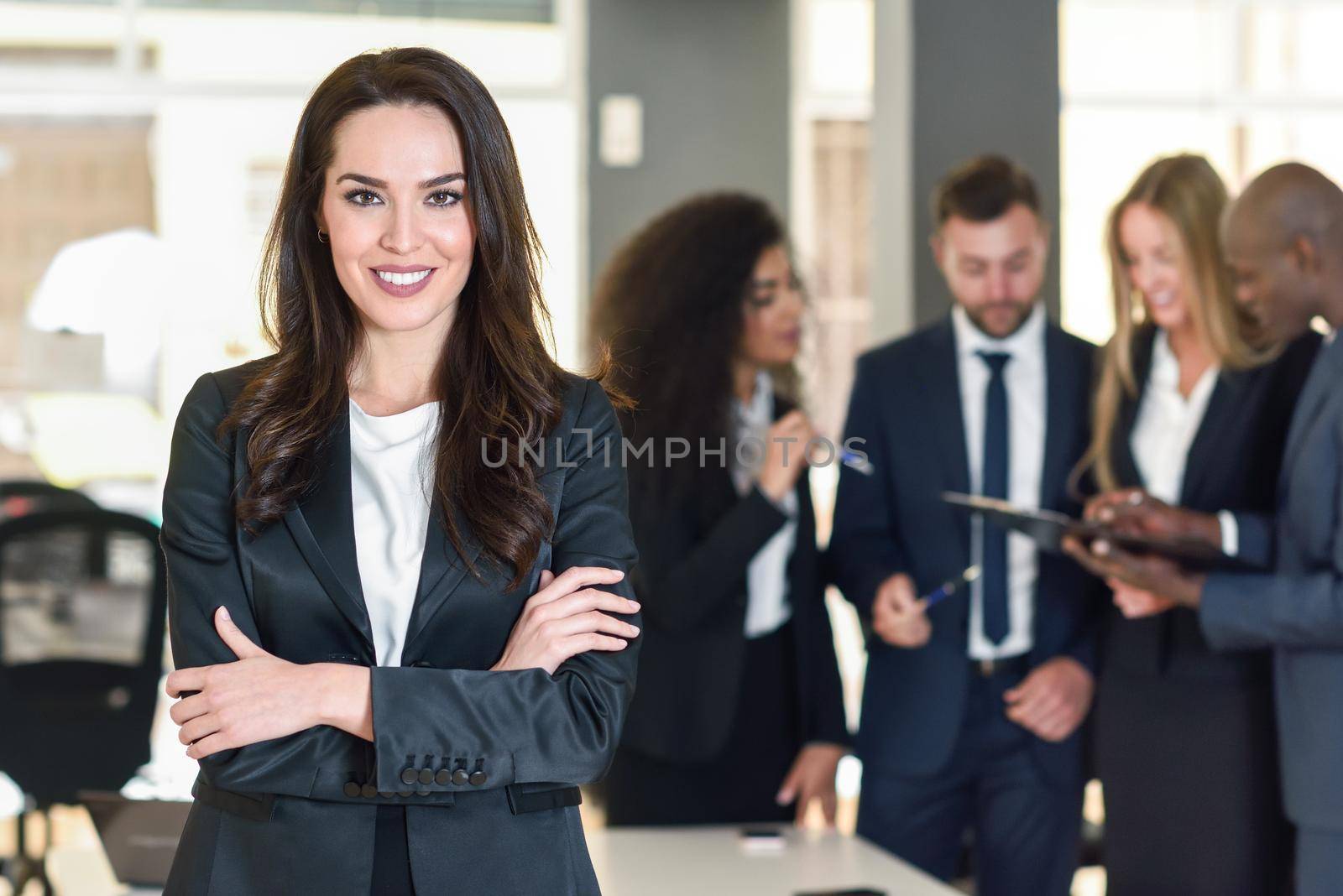 Businesswoman leader looking at camera in modern office with multi-ethnic businesspeople working at the background. Teamwork concept. Caucasian woman.