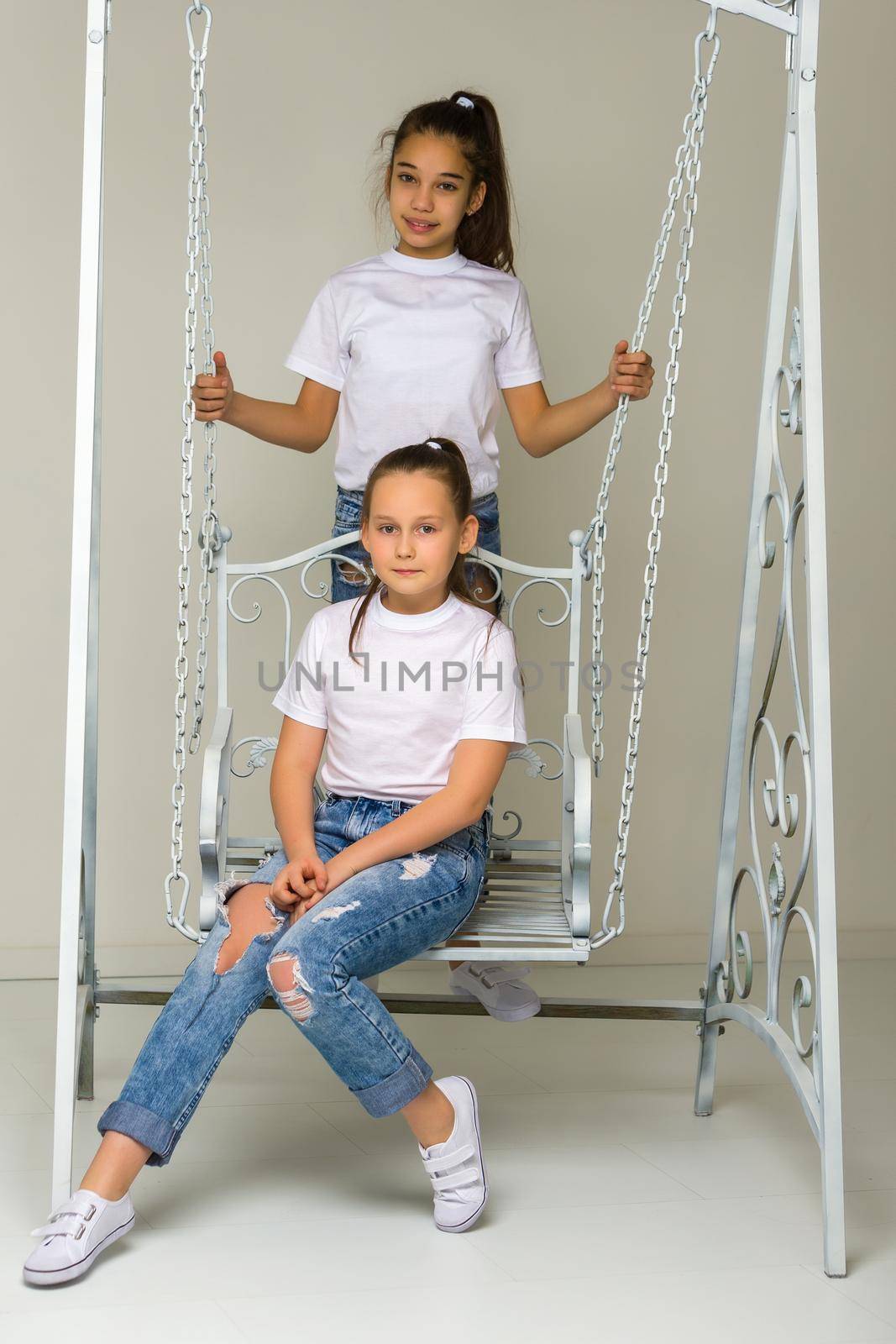 Two beautiful little girls near the swing. The concept of tenderness and beauty.