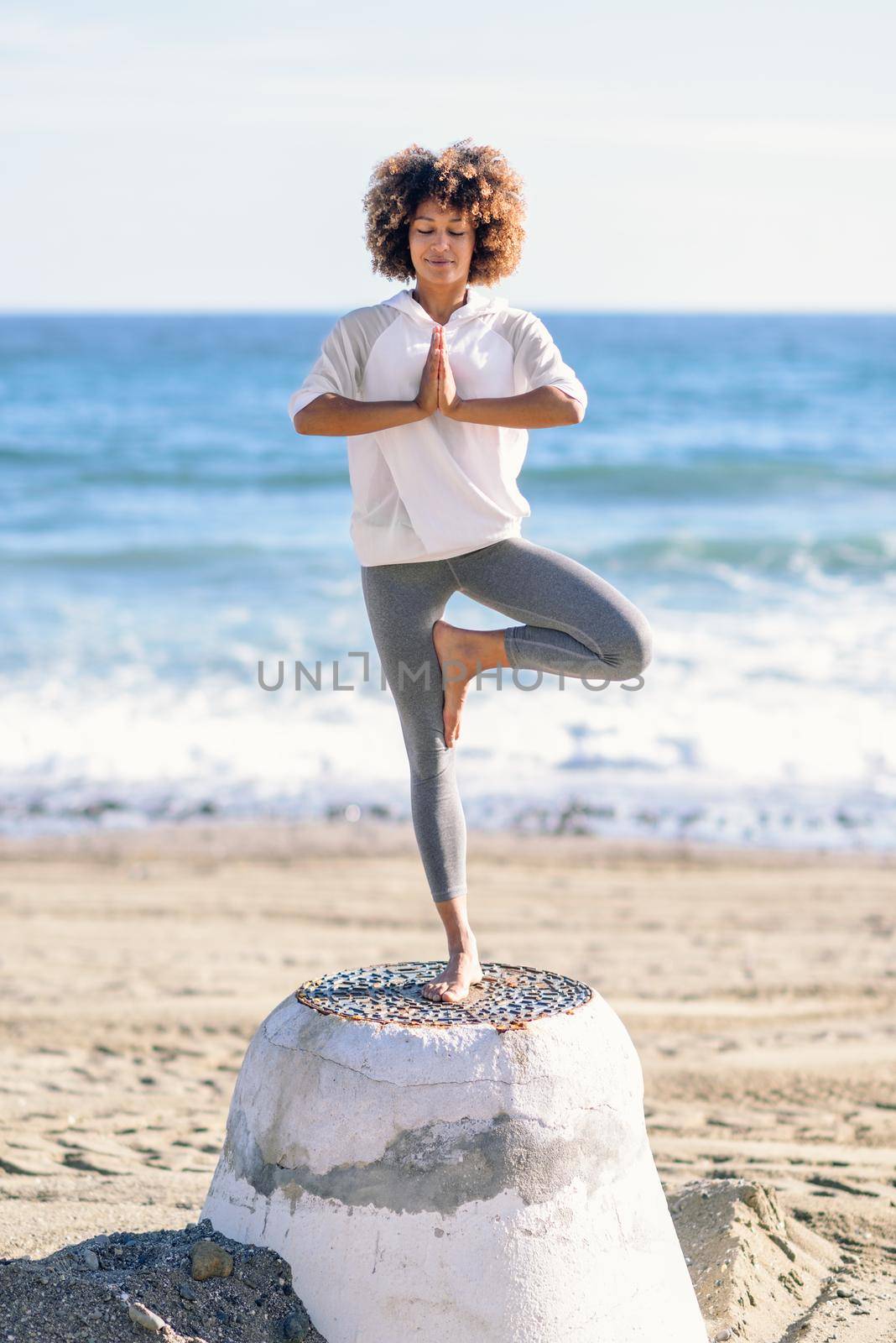 Young black woman doing yoga in the beach. by javiindy