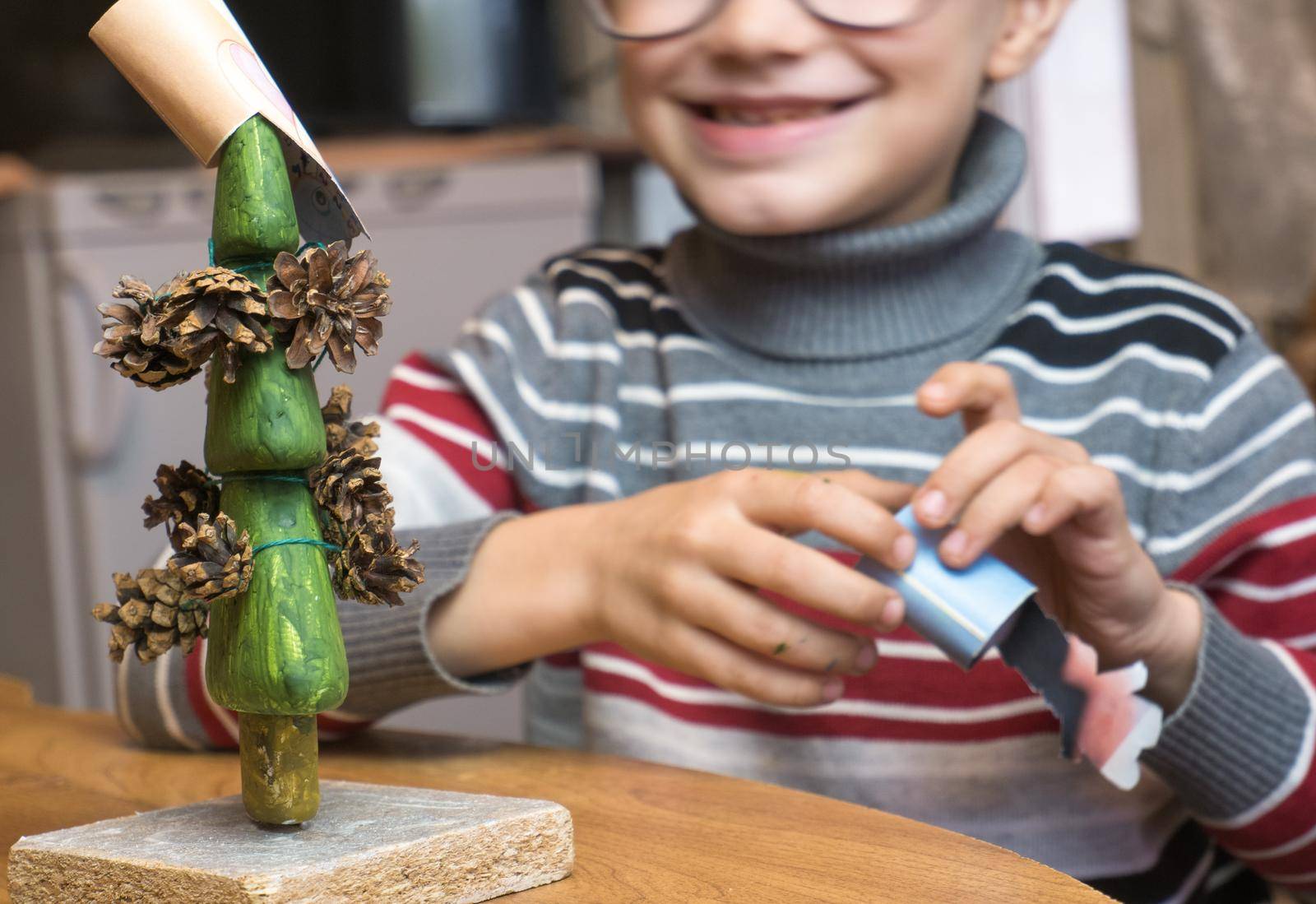 A little boy decorates a hand-made Christmas tree with pine cones and at the same time plays funny