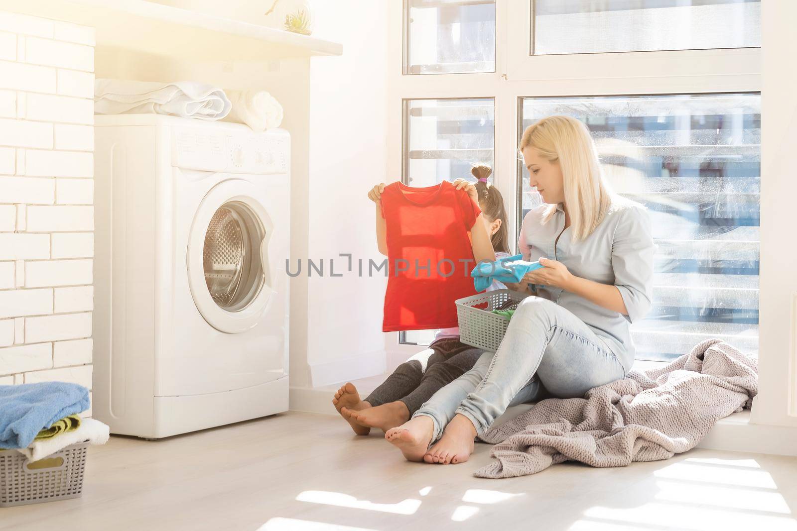 family mother and child girl little helper in laundry room near washing machine and dirty clothes