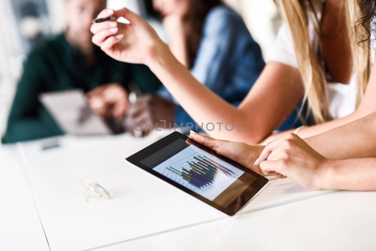 Young woman studying with tablet computer on white desk. Beautiful girls and guys working together wearing casual clothes. Coworkers group.