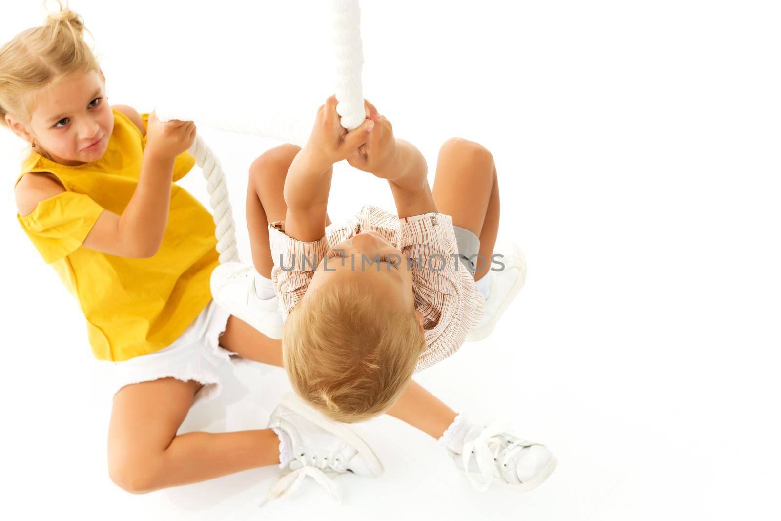 Little girl boy brother, brothers and sisters, climbs through the rope spider web, indoor obstacle quest game. The concept of active play in the home room, quarantine, self-isolation. Isolated on white background.