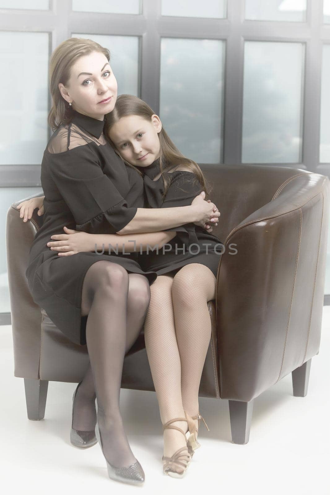 Happy family, mom and daughter near a large panoramic window, in the studio.
