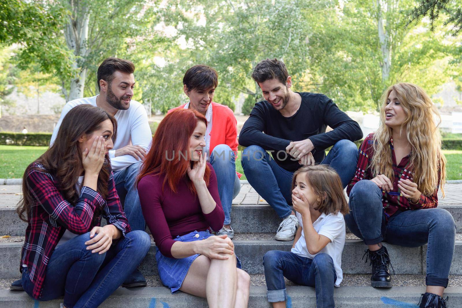 Young people together withe a little girl talking outdoors in urban background. Women and men sitting on stairs in the street wearing casual clothes.