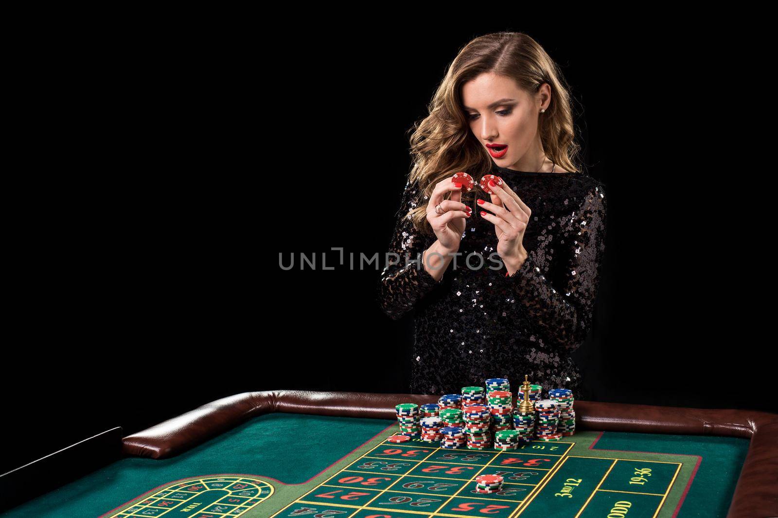 Sexy woman in a black dress playing in casino. Woman stakes piles of chips playing roulette at the casino club. Gambling. Roulette.