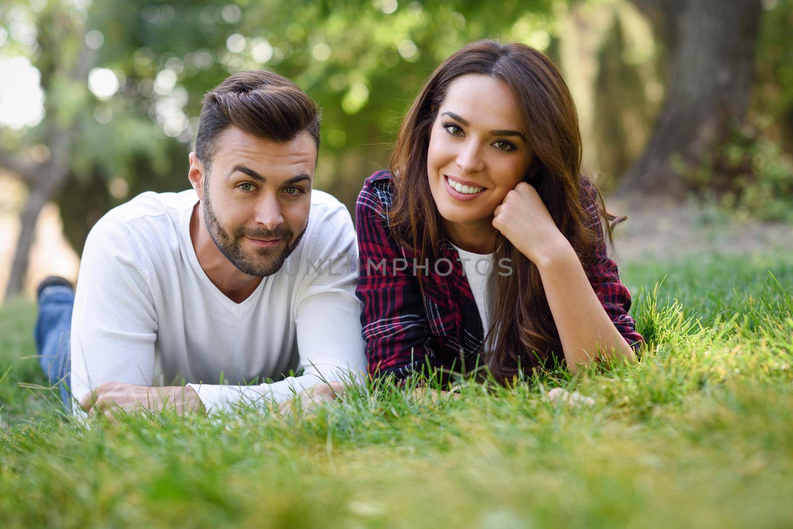 Beautiful young couple laying on grass in an urban park. Caucasian man and woman wearing casual clothes.