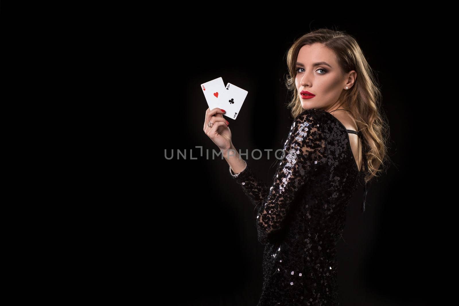 Young beautiful woman in black shiny dress holds poker cards in hands against a black background. The concept of gambling. Casino