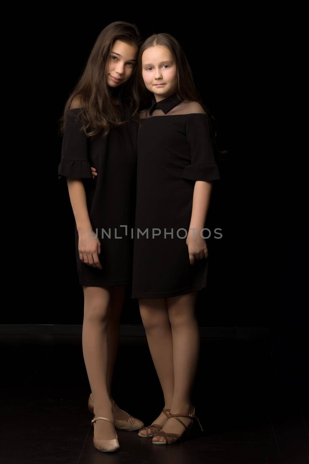 Two cute little girls posing in the studio on a black background. Style and fashion concept, layout for magazine cover.