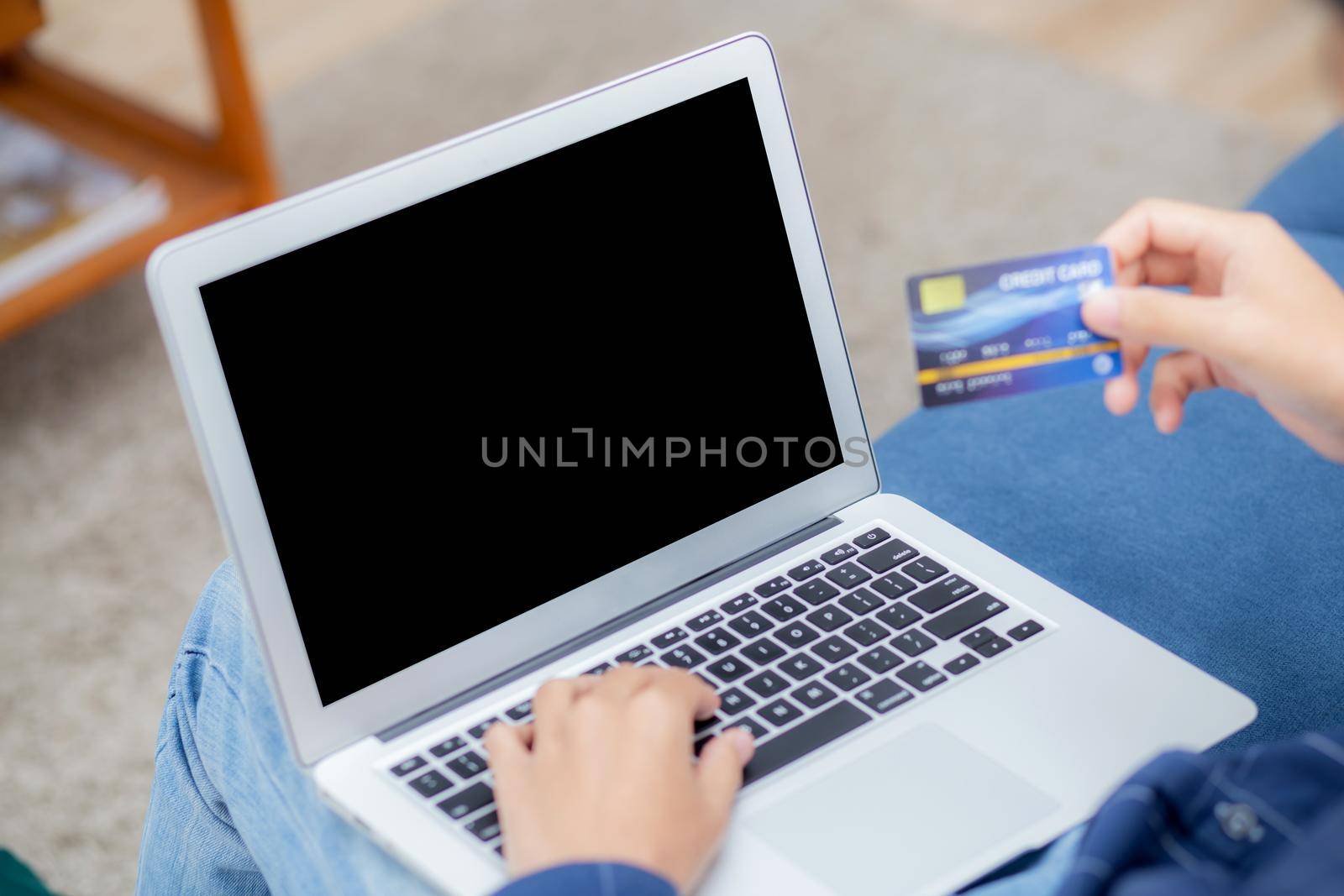Hand of young man using laptop computer display blank screen shopping online with credit card on sofa at home, male purchase and payment with debit card, e-commerce and technology, lifestyle concept.
