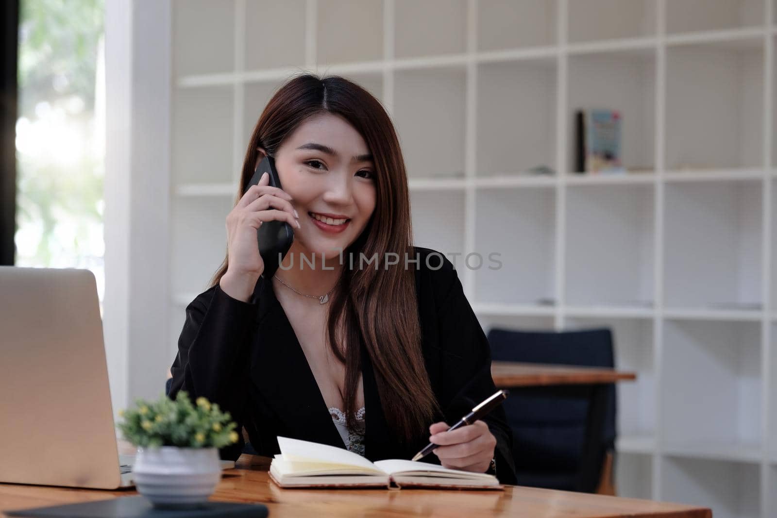 Asian business woman making a phone call and smiling look at camera. secretary famale taking note during call consultant by nateemee