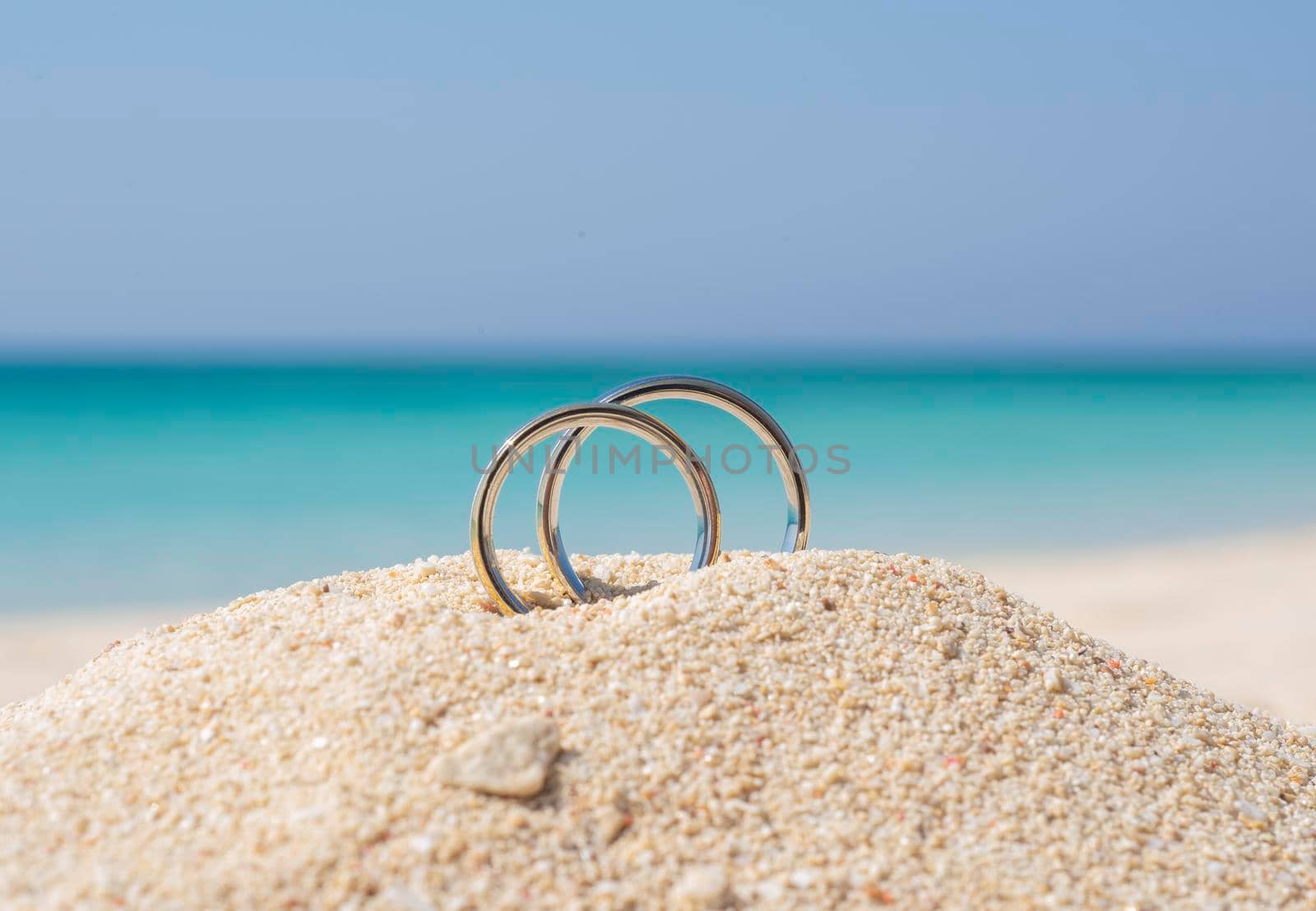 Pair wedding rings in sand on tropical beach by paulvinten