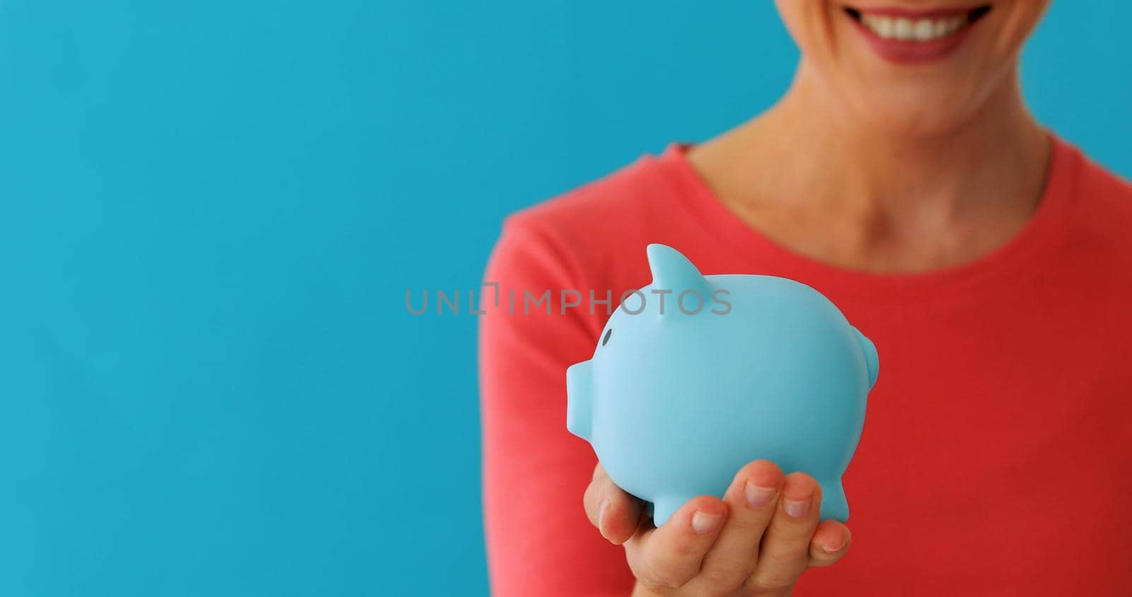 Crop positive woman in colourful clothes holding blur piggy bank over blue background