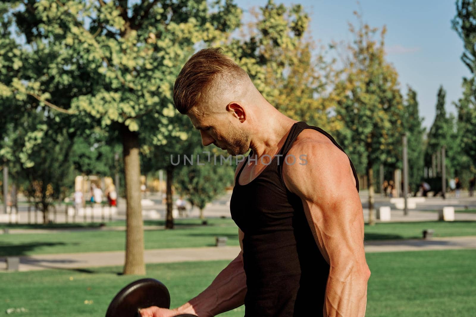 athletic man in black t-shirt with dumbbells in the park training. High quality photo