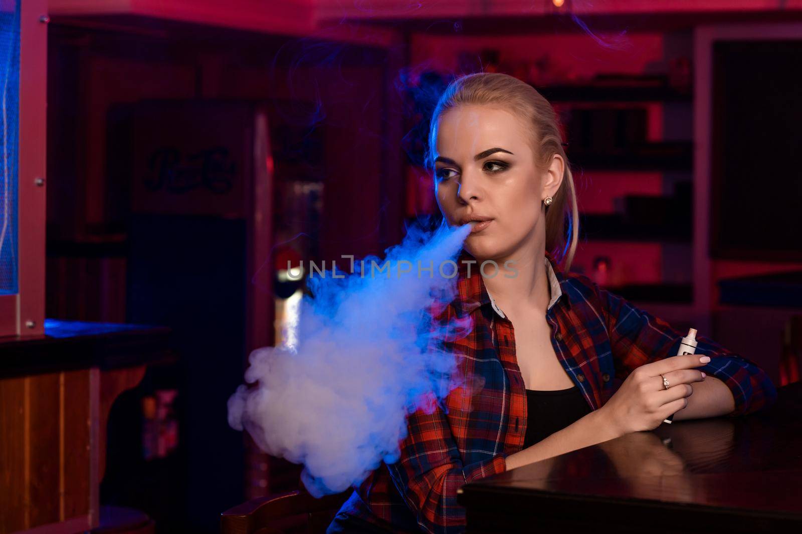 Young pretty woman in a shirt in a cage smoke an electronic cigarette at the vape bar. Vape shop.
