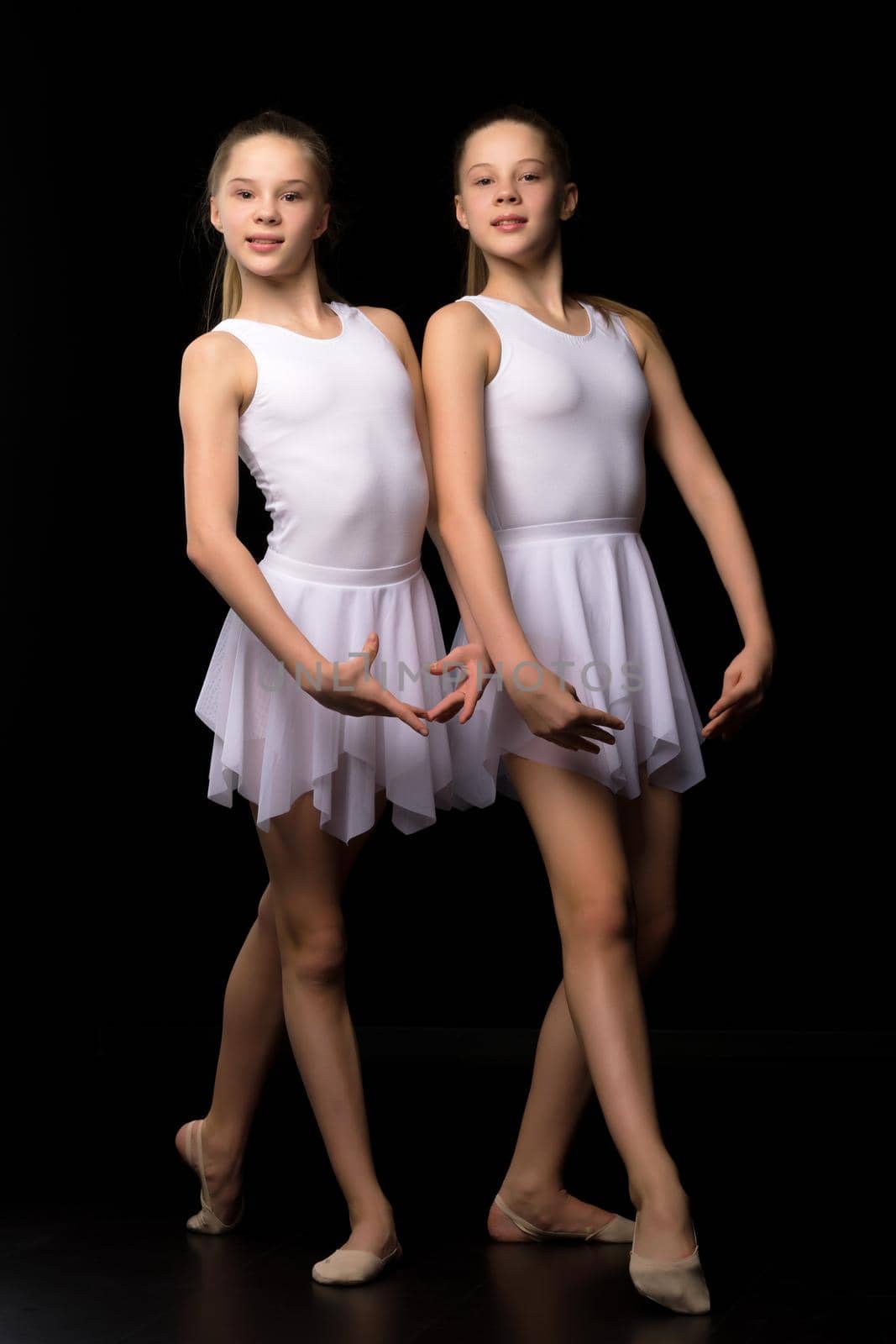 Two charming gymnasts in beautiful sports swimsuits posing in the studio. The concept of children's sports, fitness. Isolated on a black background.