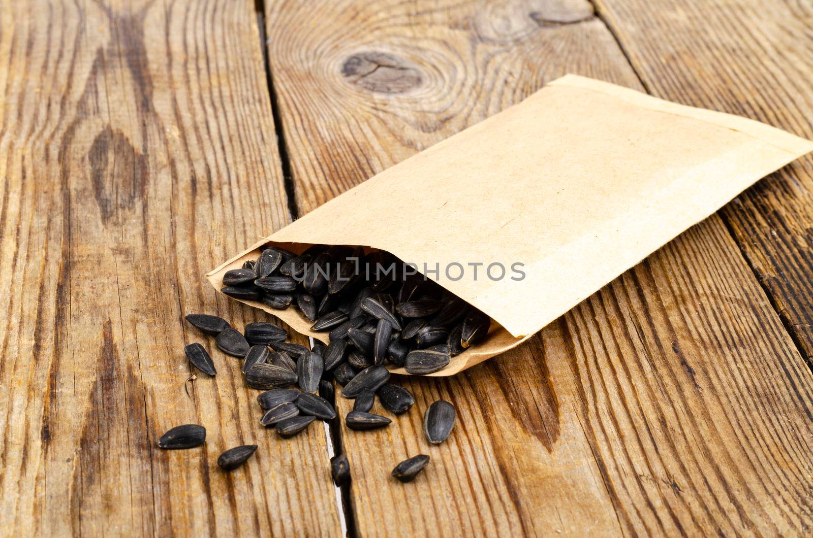 Black unpeeled sunflower seeds in craft bag on wooden table. Studio Photo