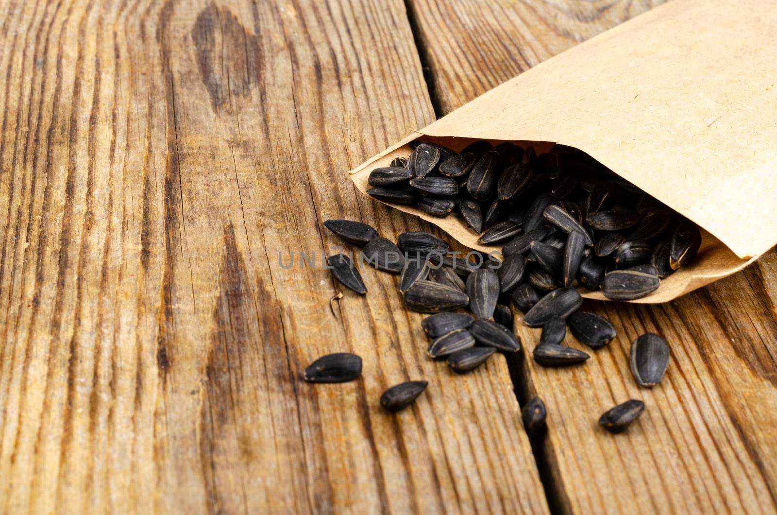 Black unpeeled sunflower seeds in craft bag on wooden table. by ArtCookStudio