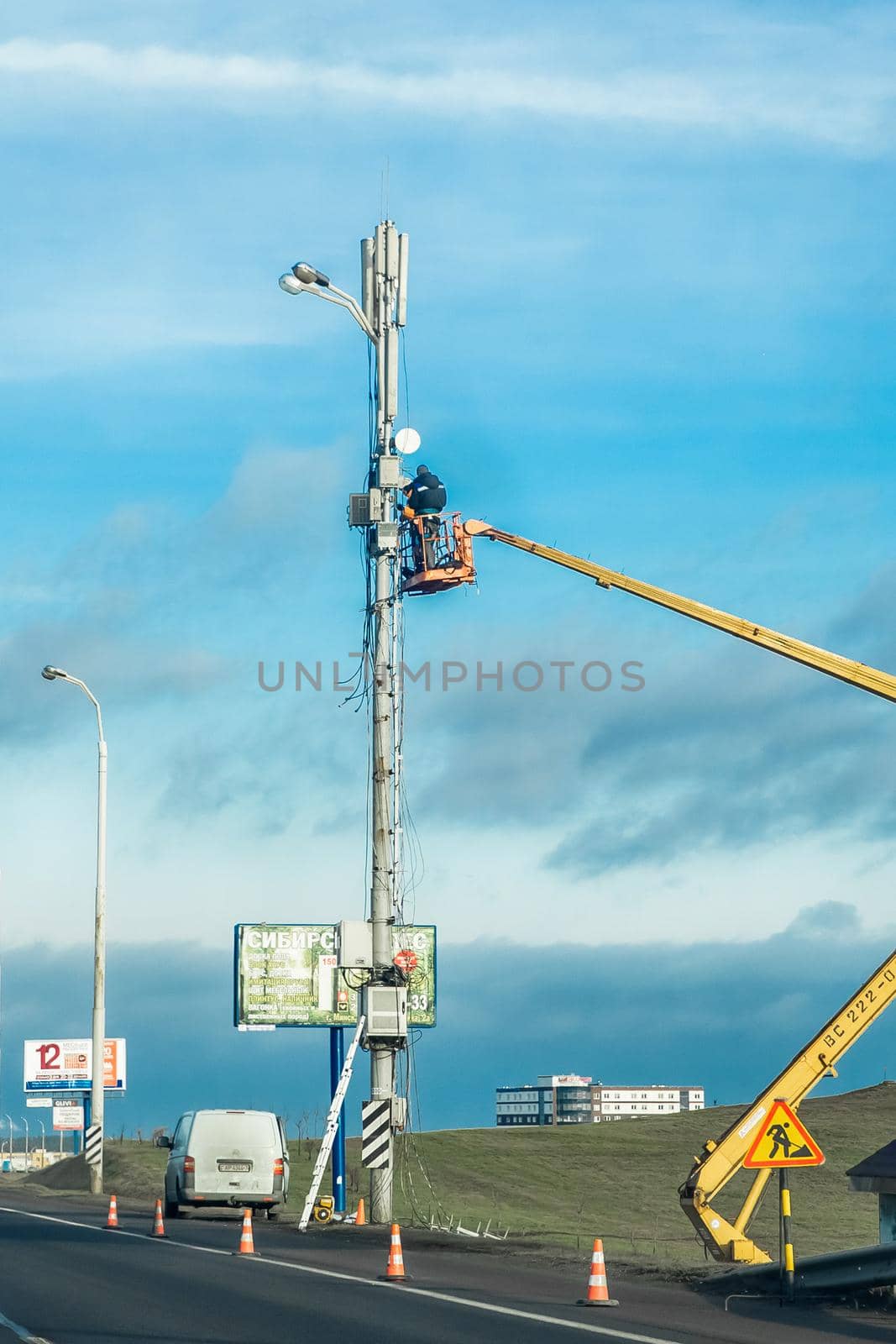 Belarus, Minsk - December 19, 2019: Industrial working men raised on a machine crane mending a power line by AYDO8