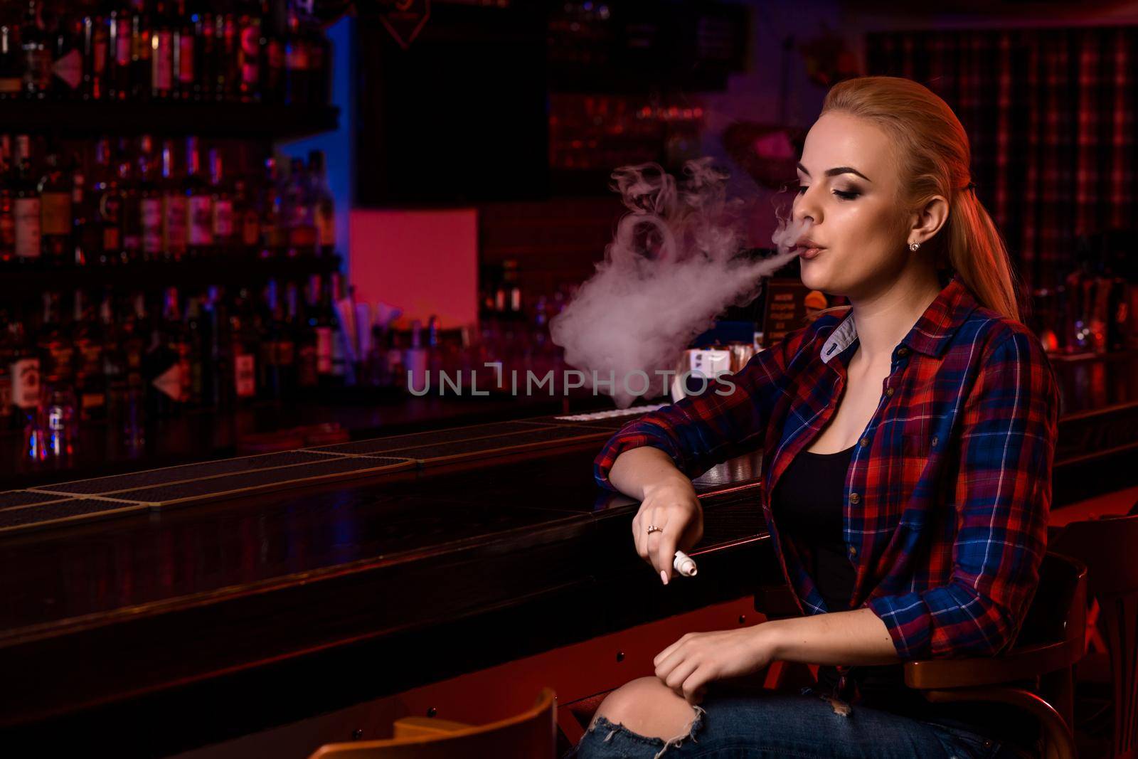 Young pretty woman smoke an electronic cigarette at the vape bar. Vape shop.
