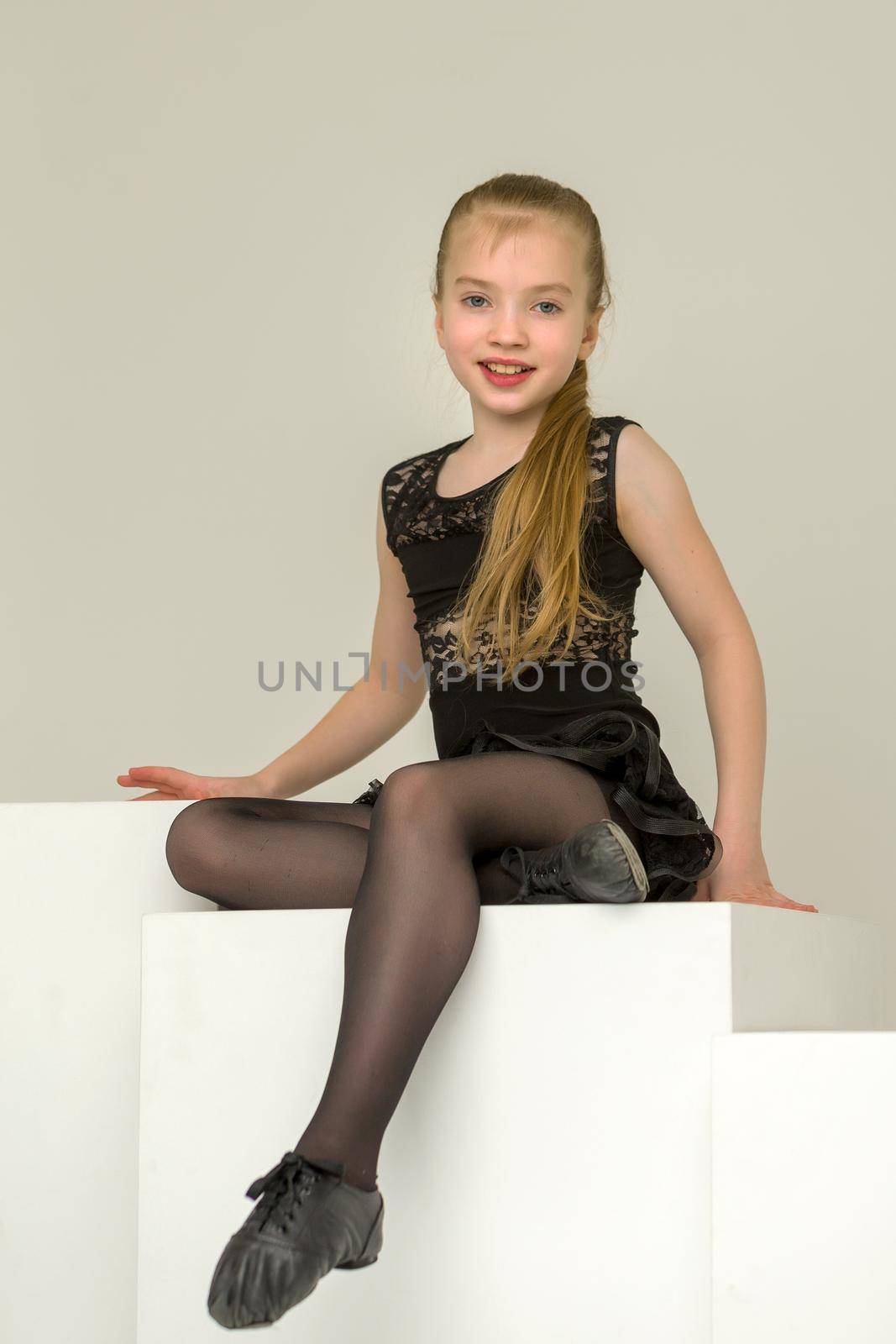 Little girl in dance costume posing in studio on a white cube. by kolesnikov_studio