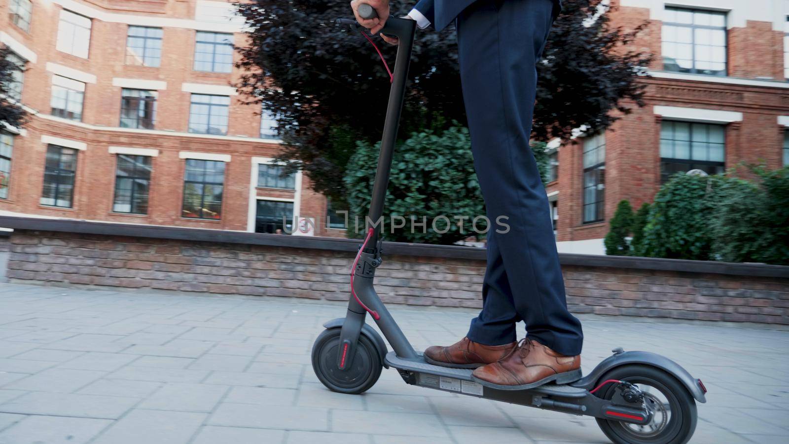 Executive manager riding electric scooter moving forward along startup company office building. Businessman in diplomatic suit going at home after working day. Concept of eco-friendly transportation