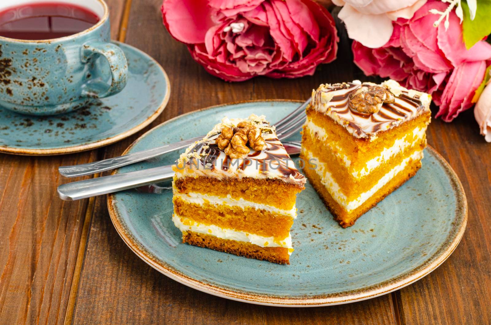 Two pieces of carrot cake on blue plate, cup of tea on wooden table. Studio Photo