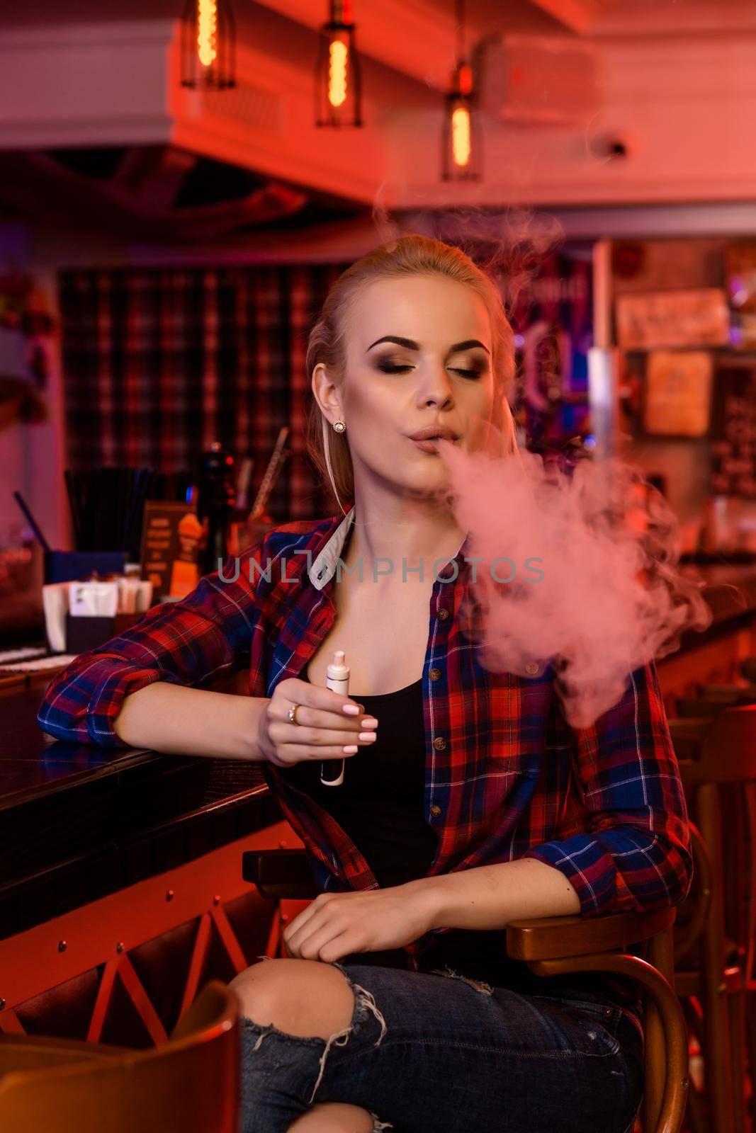 Young pretty woman smoke an electronic cigarette at the vape bar. Vape shop.