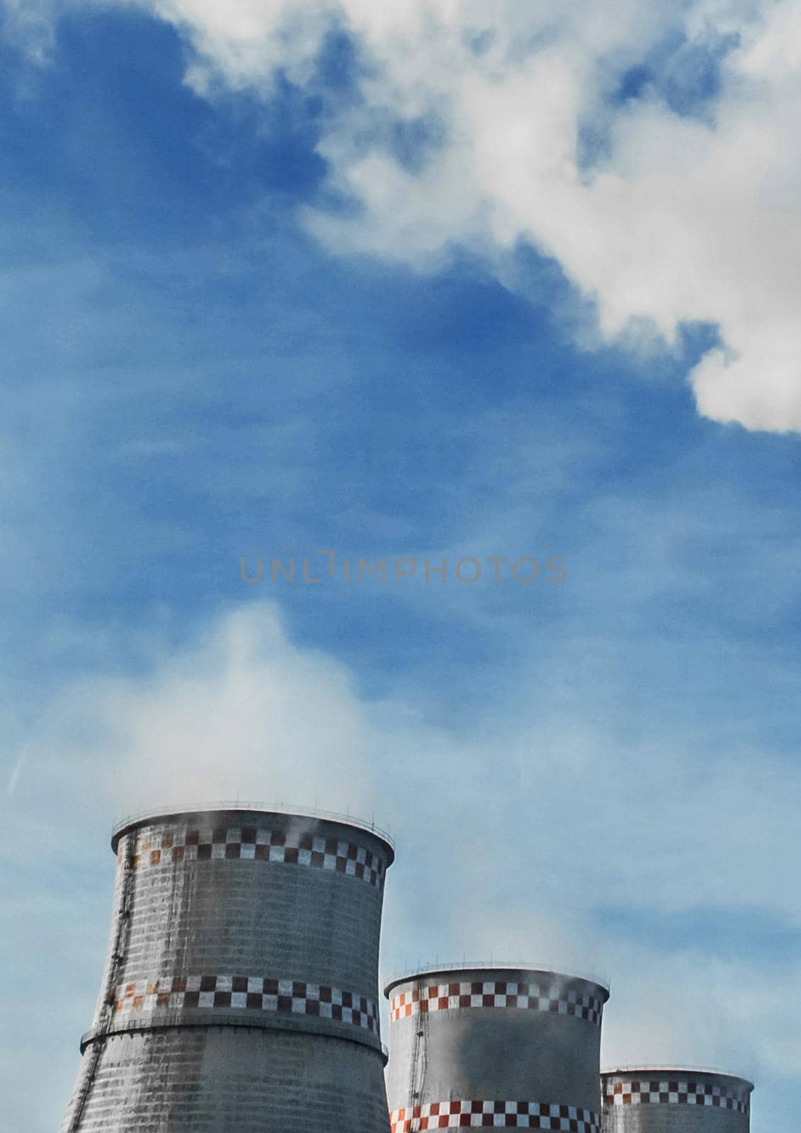 Cooling tower and smoke of an industrial plant or thermal power plant against a blue sky.