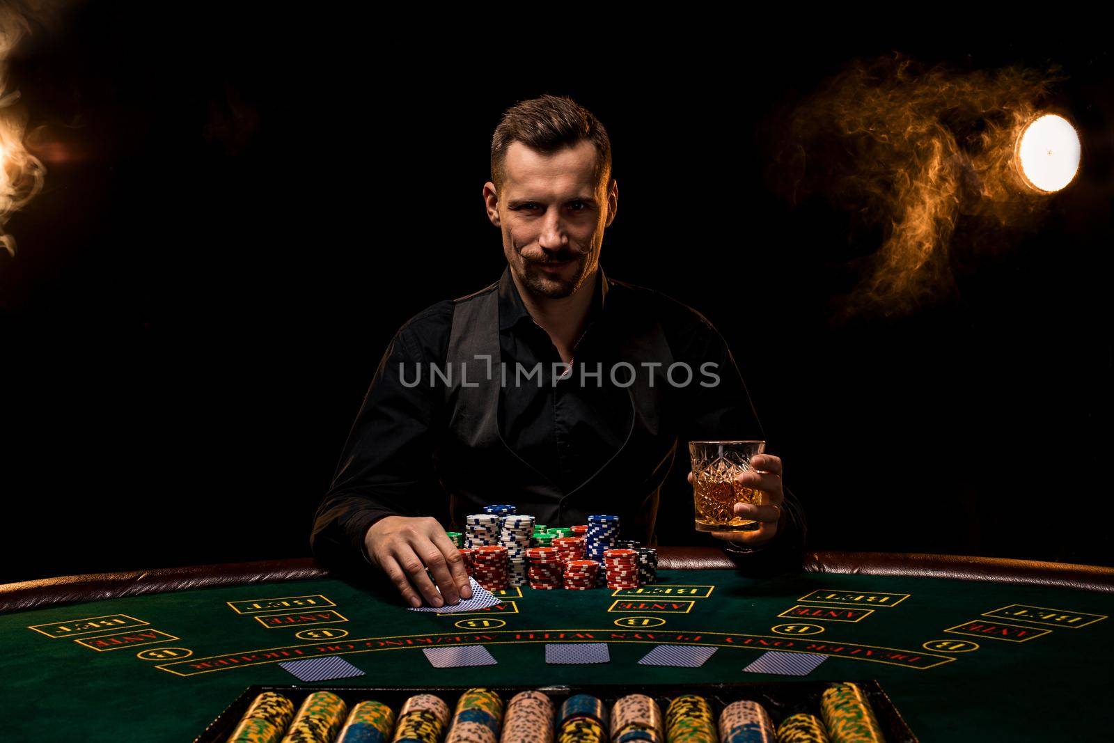 Poker player. Young guy in the casino at the gaming table. Man gambling, card games. Cards, chips, whiskey, cigarettes, poker, card game, gambling - gambling concept. Black background