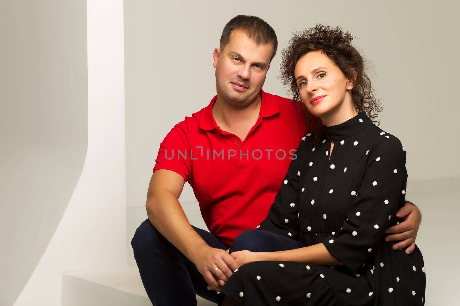 Beautiful family man and woman are sitting on the white stairs in the studio. The concept of love, friendship.