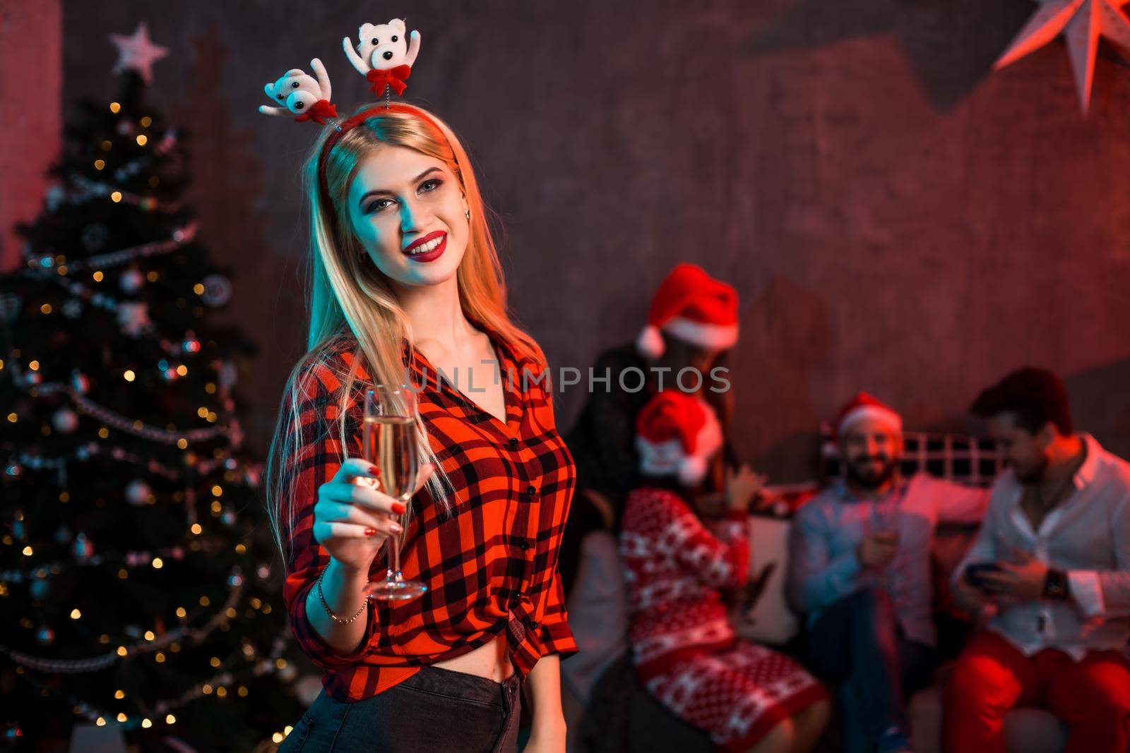 Beautiful young woman with glass of champagne at Christmas party. Funny people.