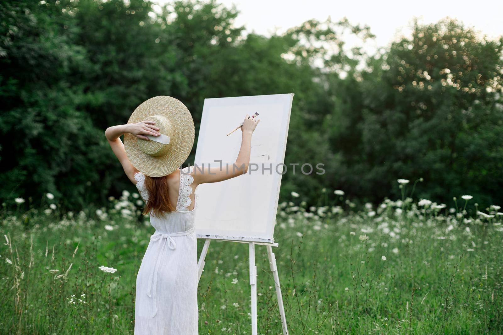 A woman in a white dress in a field with flowers paints a picture by Vichizh