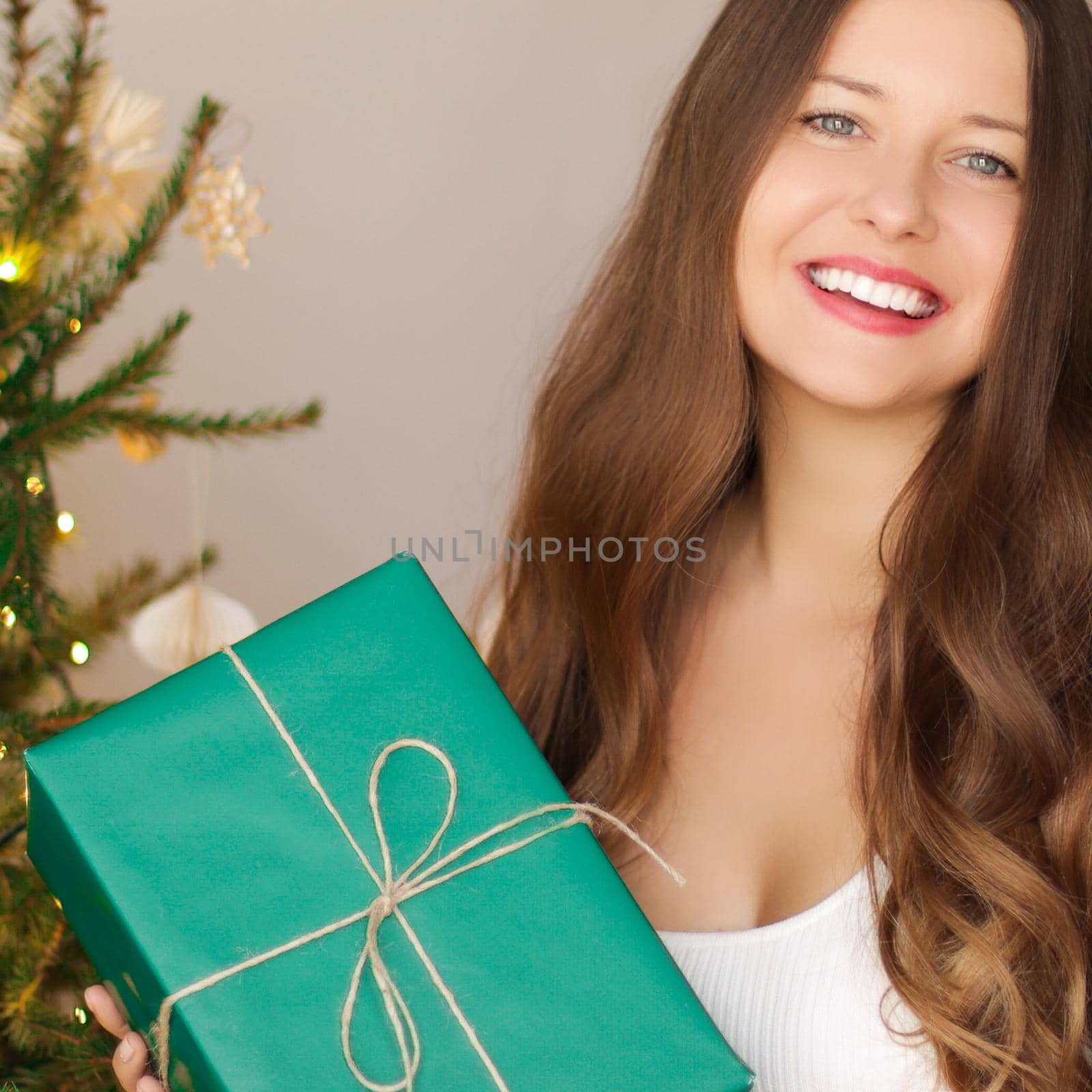Christmas holiday and sustainable gifts concept. Happy smiling woman holding wrapped present with eco-friendly green wrapping paper by Anneleven