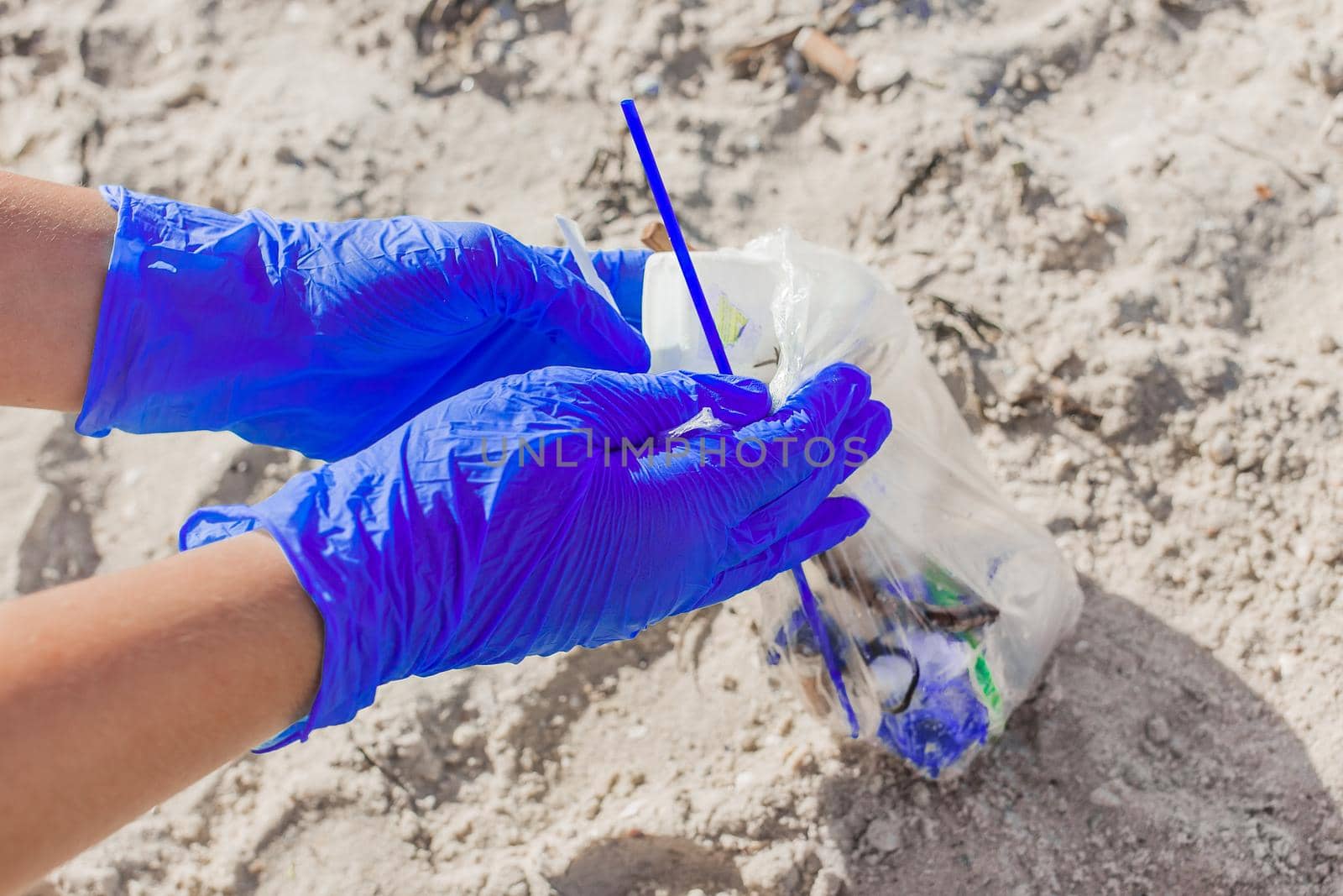 Hands of a girl in blue household gloves collect garbage in a bag on the beach close-up cleaning plan.