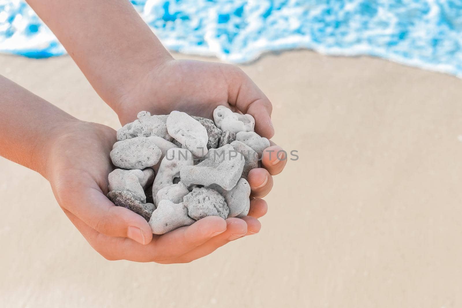 Man's hands hold pile of grey stones amid seashore close-up.