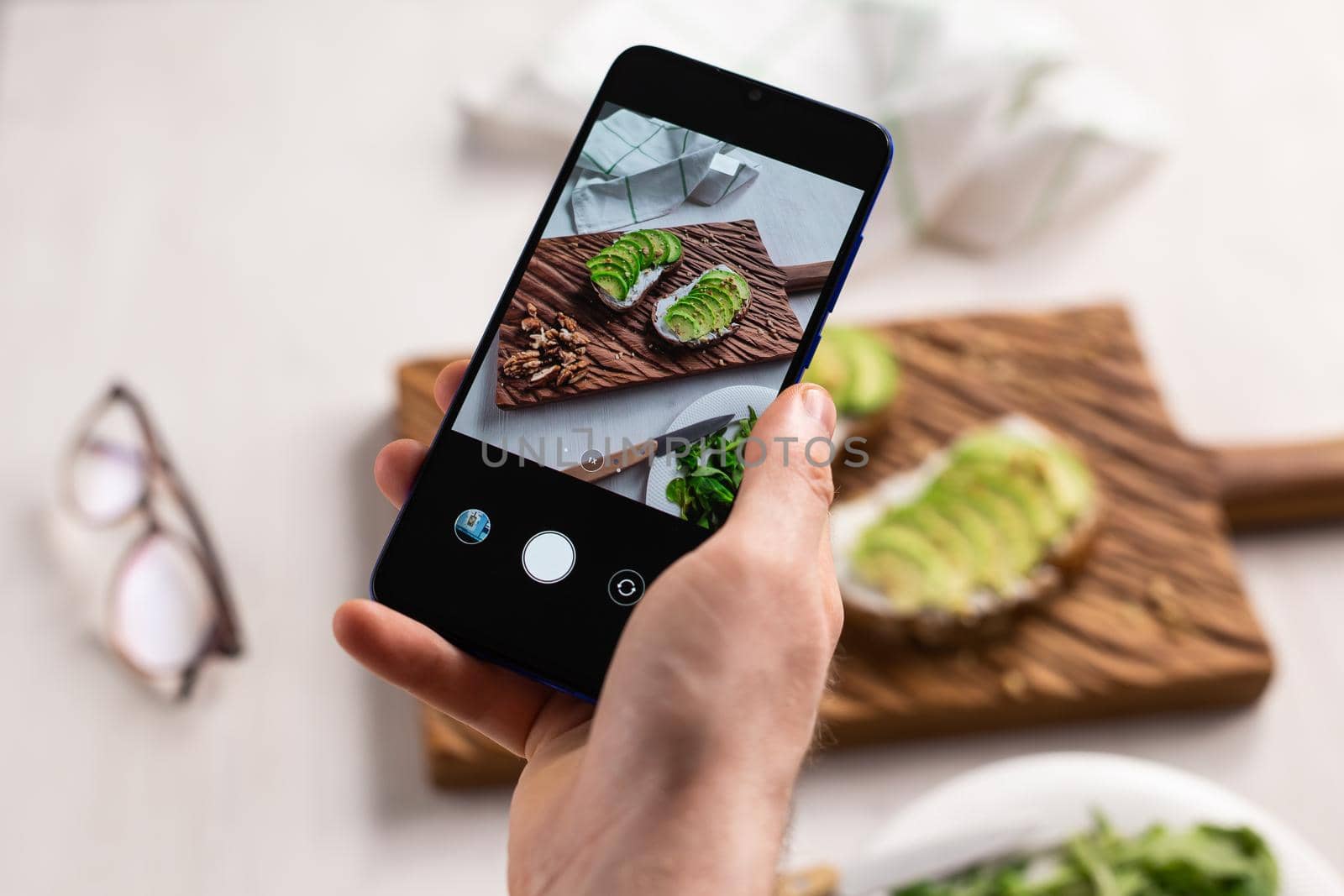 Hands take pictures on smartphone of two beautiful healthy sour cream and avocado sandwiches lying on board on the table. Social media and food