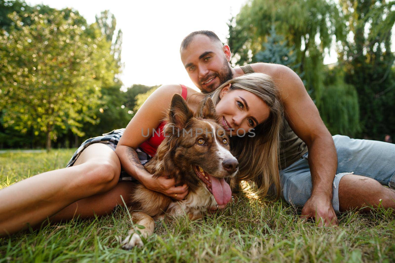 Young happy couple playing with their dog smiling in park, close up