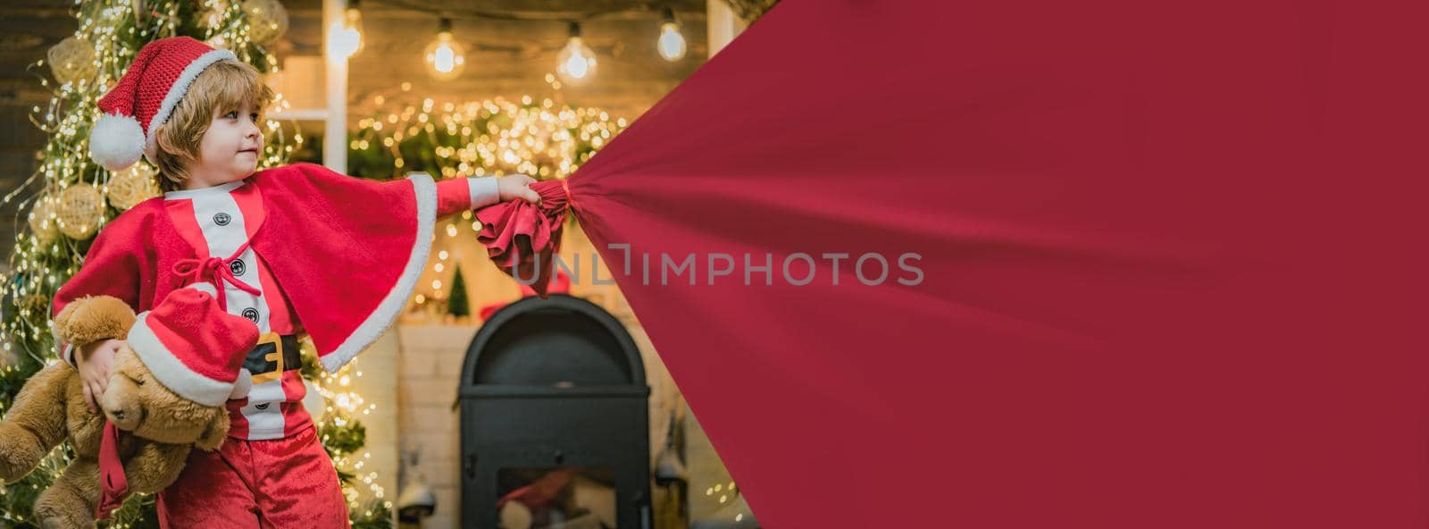 Santa child pulling huge bag of gifts, banner isolated on red background with copy space. Adorable child play with bag full of presents on christmas tree at home